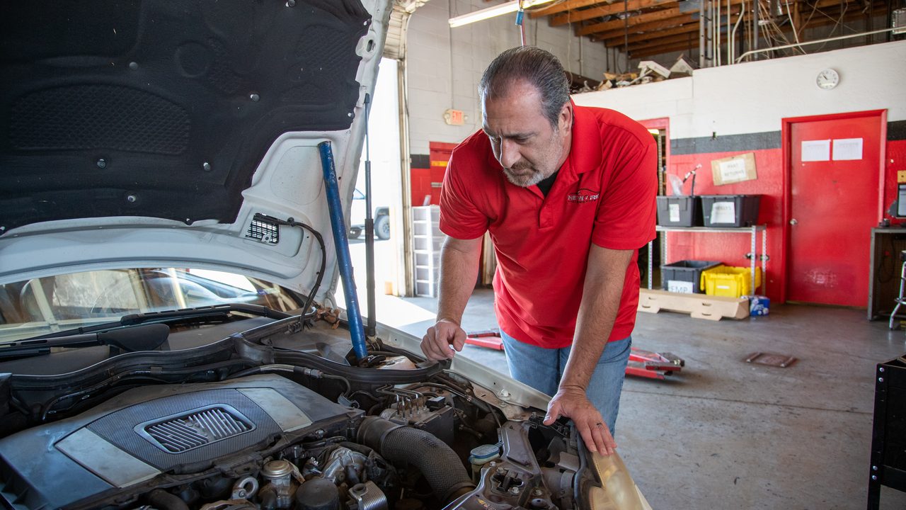A technician inspects the engine bay of a car inside an auto repair shop