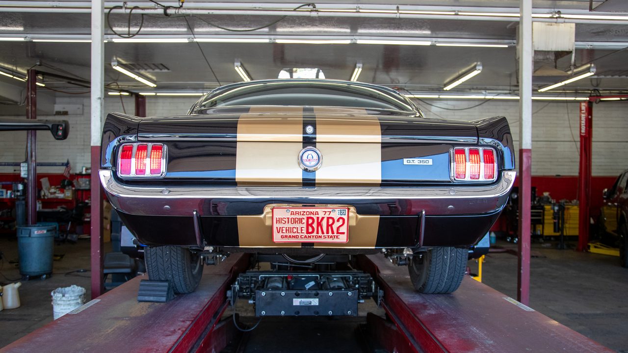 A classic Shelby GT350 sports car rests on a drive-on lift inside an auto repair service bay