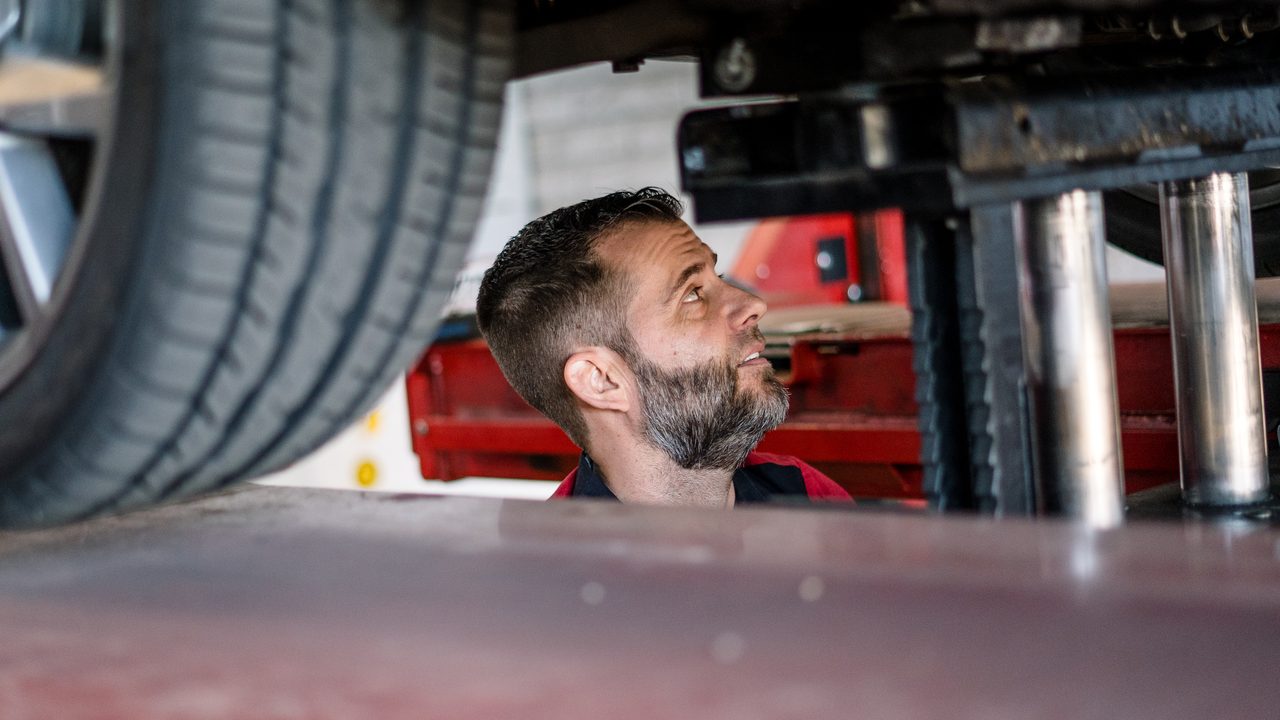 A technician inspects the undercarriage of a vehicle elevated on a service lift