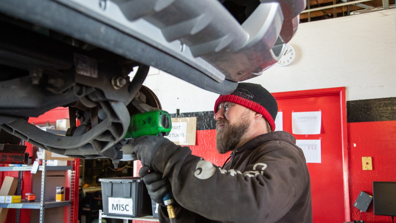 A technician uses a power tool to work on the front suspension of a vehicle