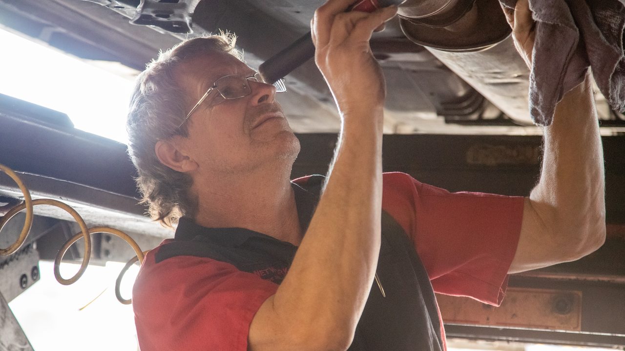 A technician uses a flashlight to inspect the undercarriage and exhaust system of a raised vehicle