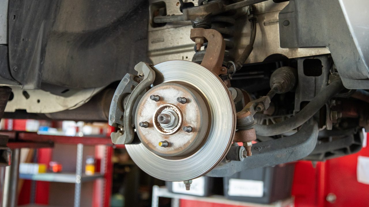 A vehicle's front suspension, brake rotor, and caliper are exposed on a lift in a service bay