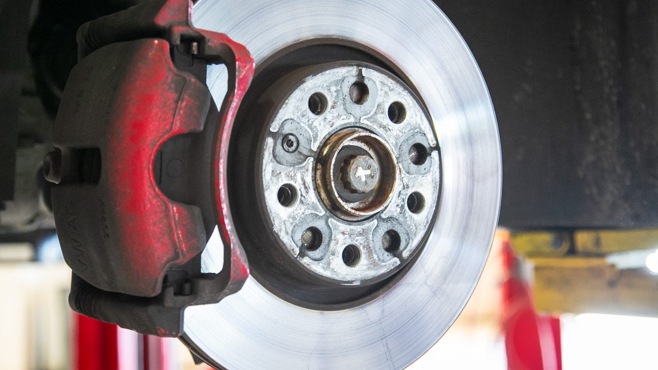 A close-up view of a vehicle's brake rotor and red brake caliper raised on a shop lift