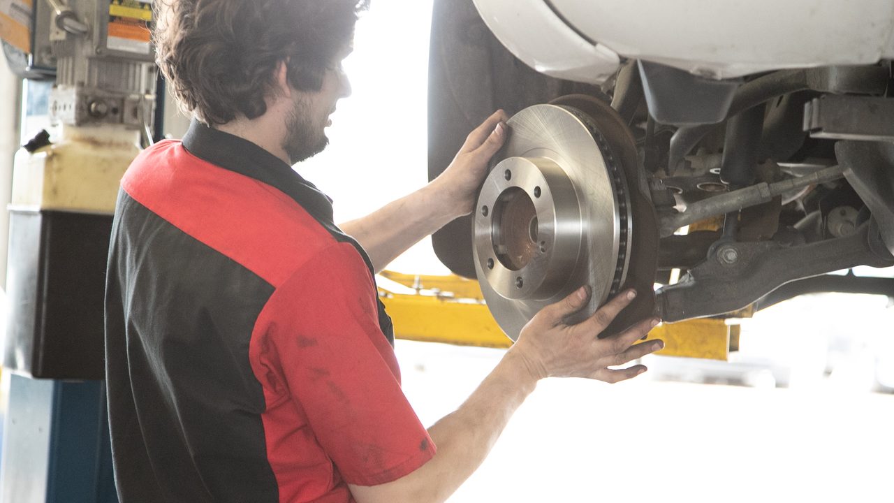 A technician installs a new brake rotor on a vehicle elevated on a lift in a service bay