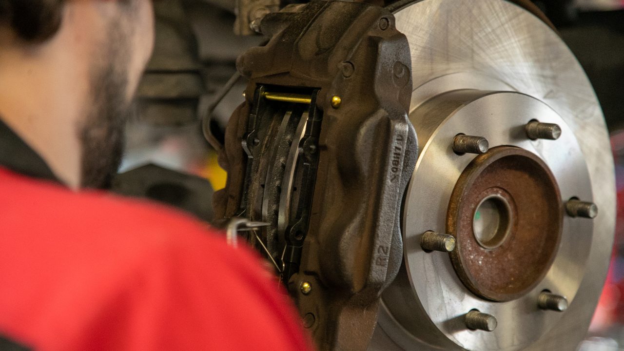 A technician installs new brake pads into a brake caliper on a vehicle's wheel hub