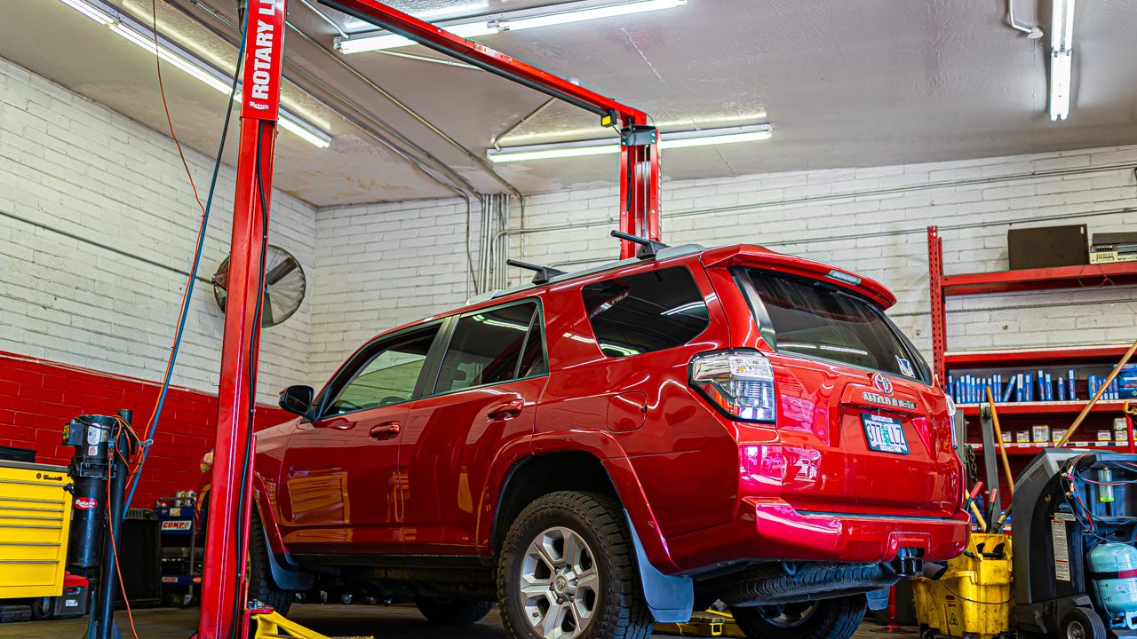 A red SUV sits positioned on a two-post lift inside an auto repair service bay
