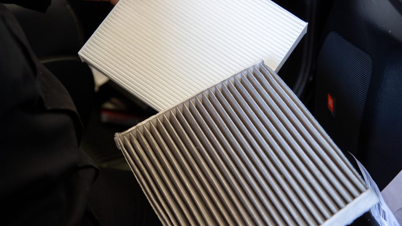 A technician compares a dirty used cabin air filter with a clean new replacement filter
