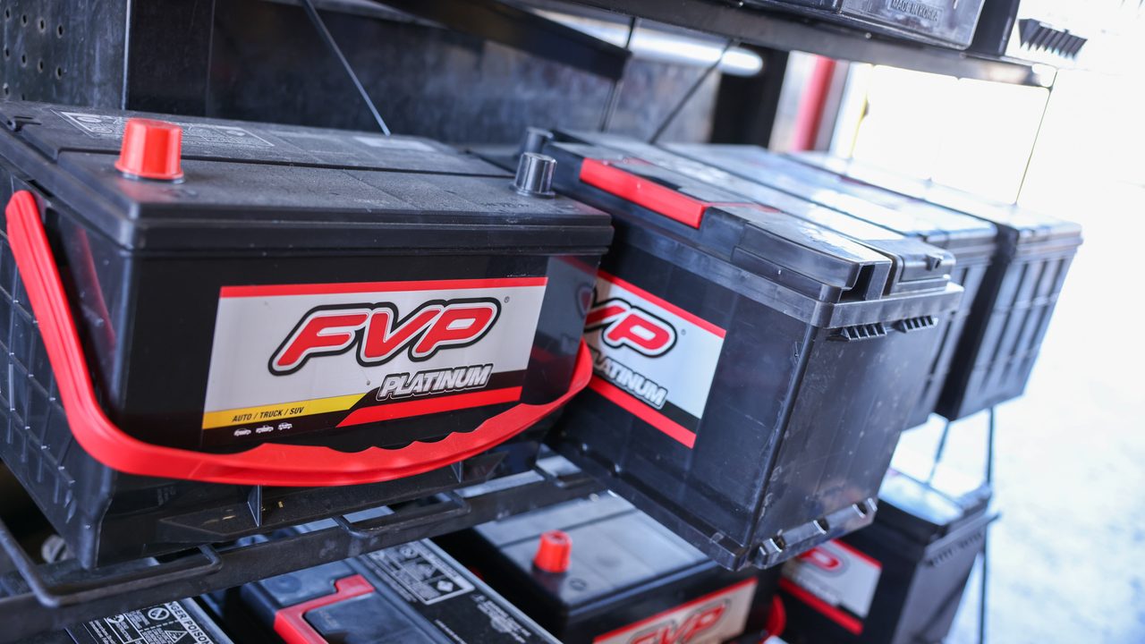 New automotive replacement batteries sit stocked on a metal storage rack inside a repair shop