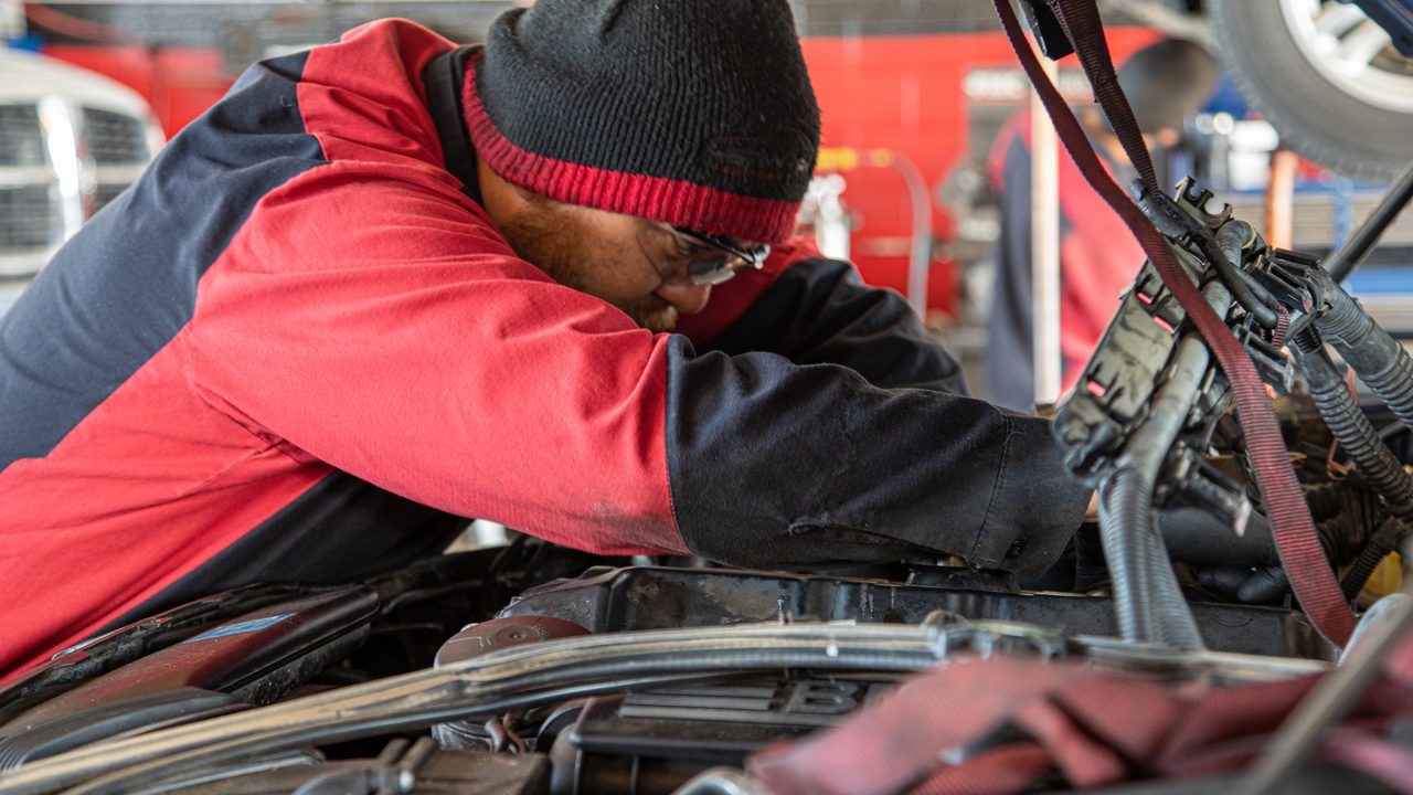 A technician leans into an open engine bay to perform repair work on a vehicle