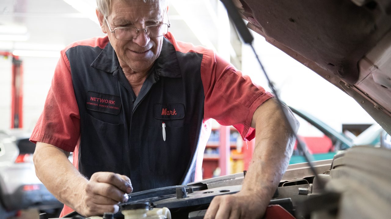 A technician inspects components inside a vehicle's engine bay under the open hood