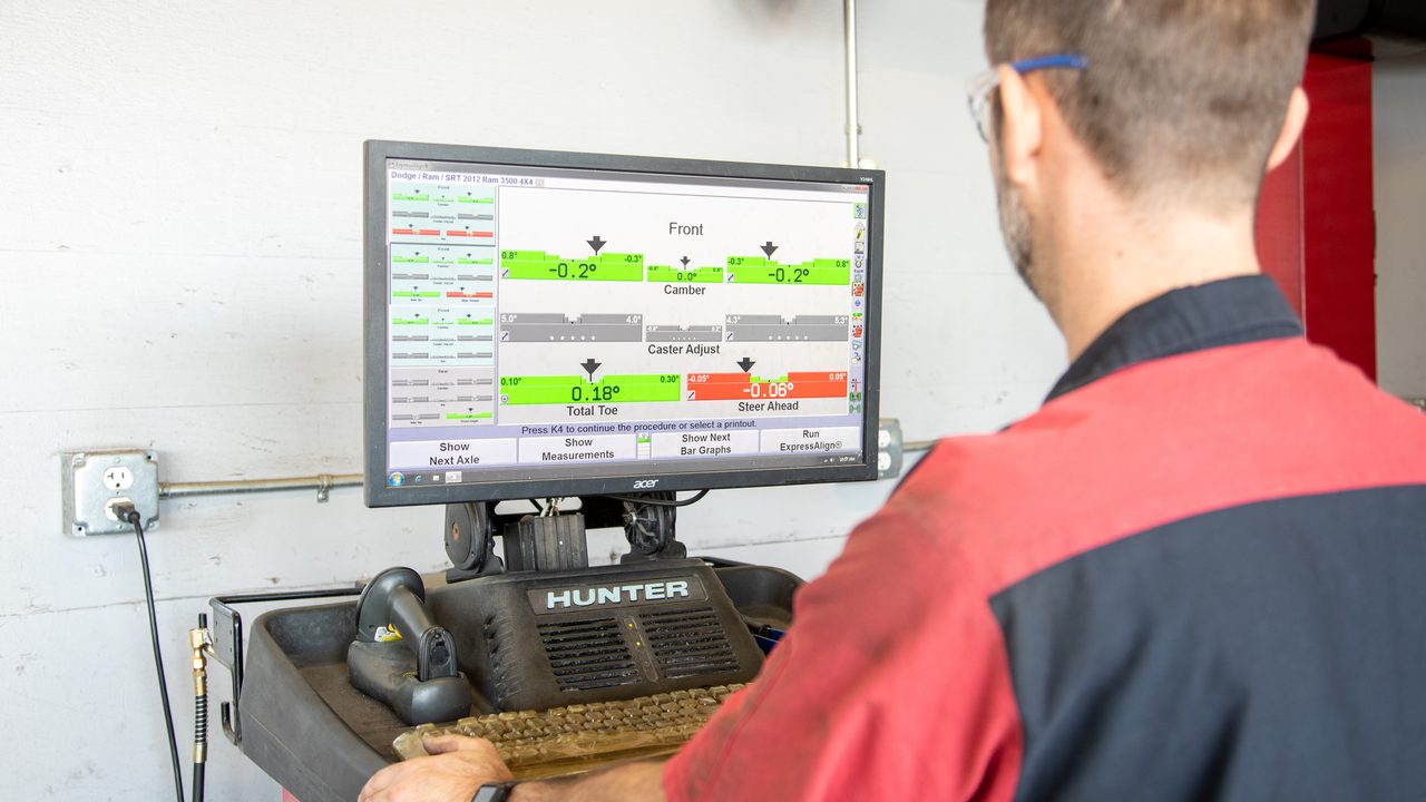 A technician reviews wheel alignment measurements on a computer screen in a service bay
