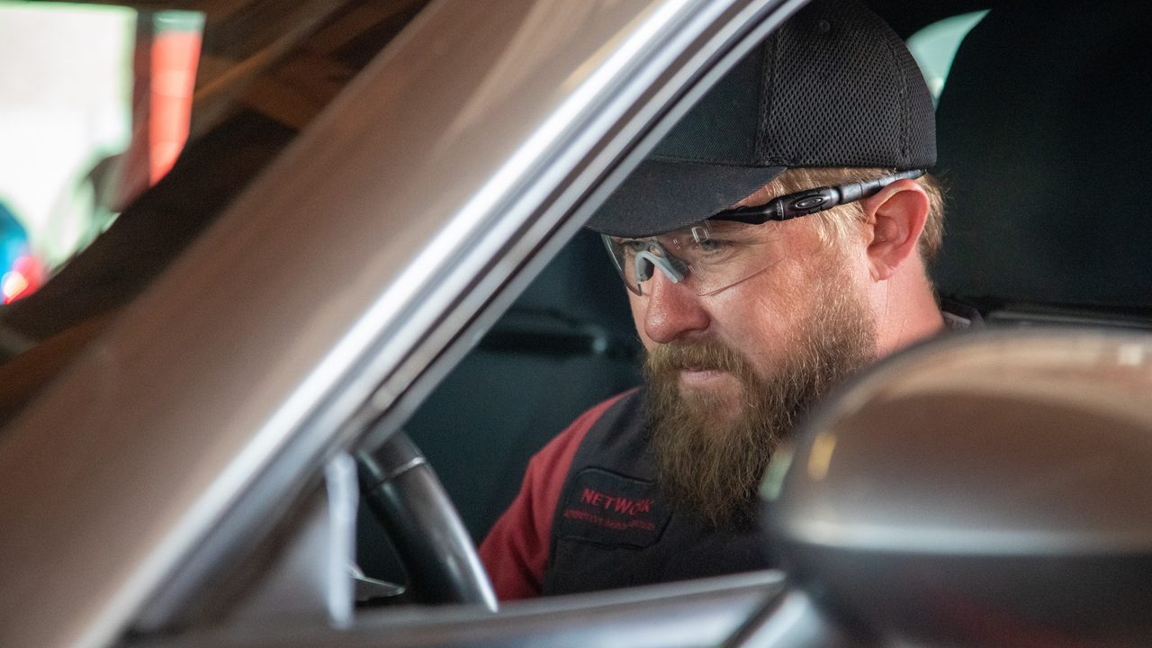 A technician sits behind the steering wheel inside a vehicle to conduct an inspection