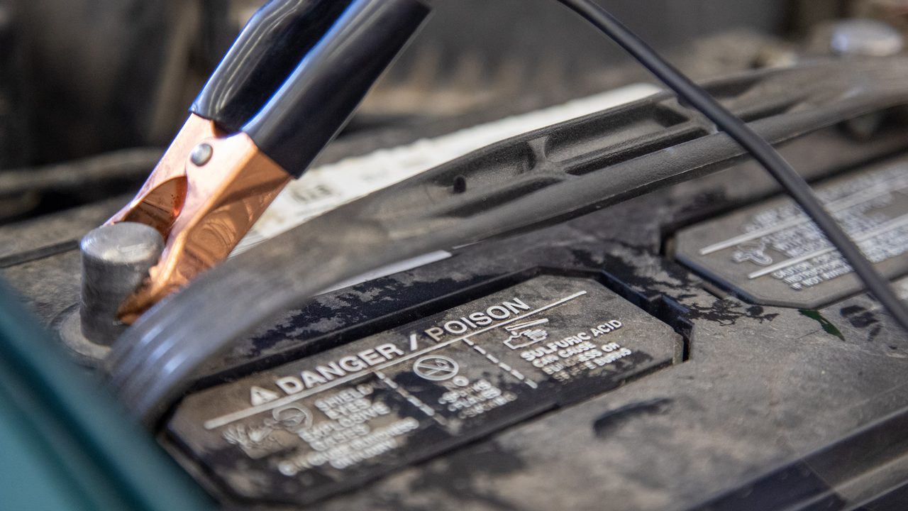 A jumper cable clamp is connected to a terminal of a car battery in an engine bay