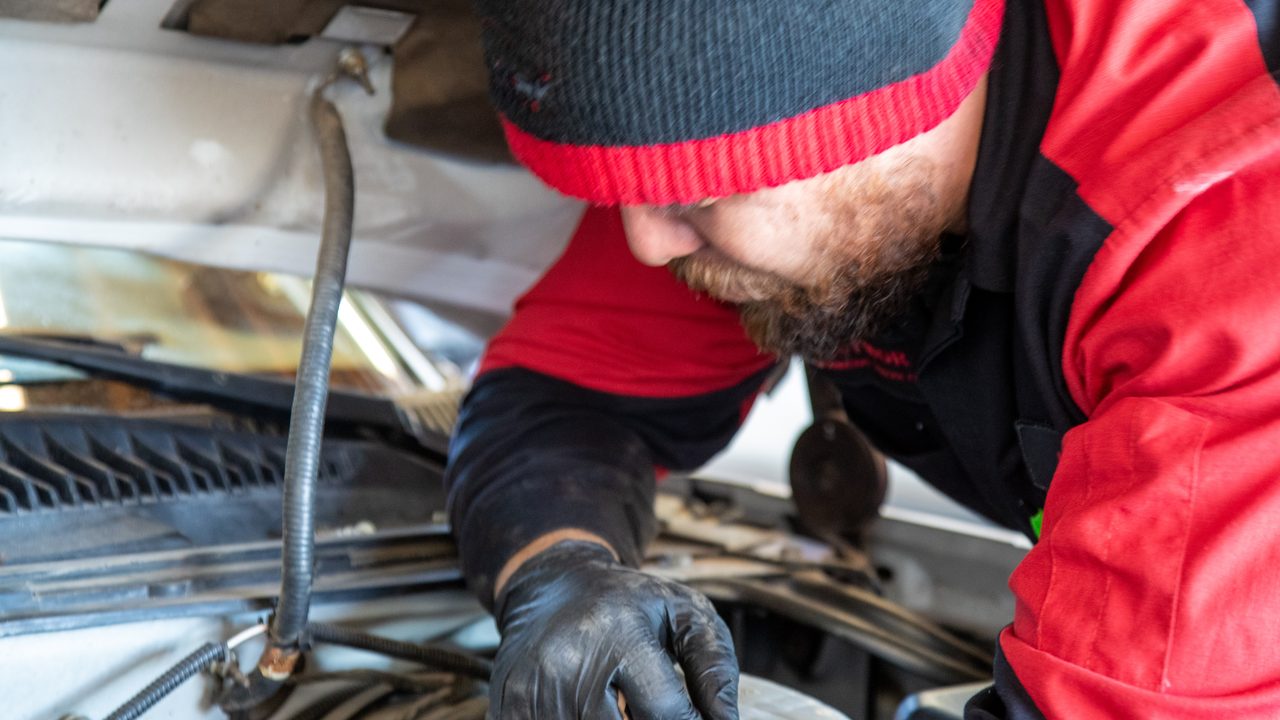 A technician wearing gloves inspects components inside an open engine bay