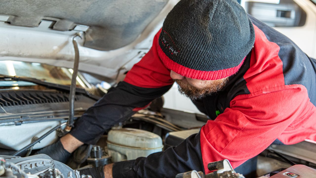 A technician leans into the engine bay of a truck to perform repairs