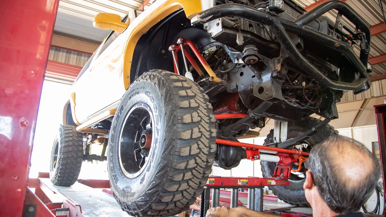 A technician inspects the modified suspension and undercarriage of a lifted truck on an alignment rack