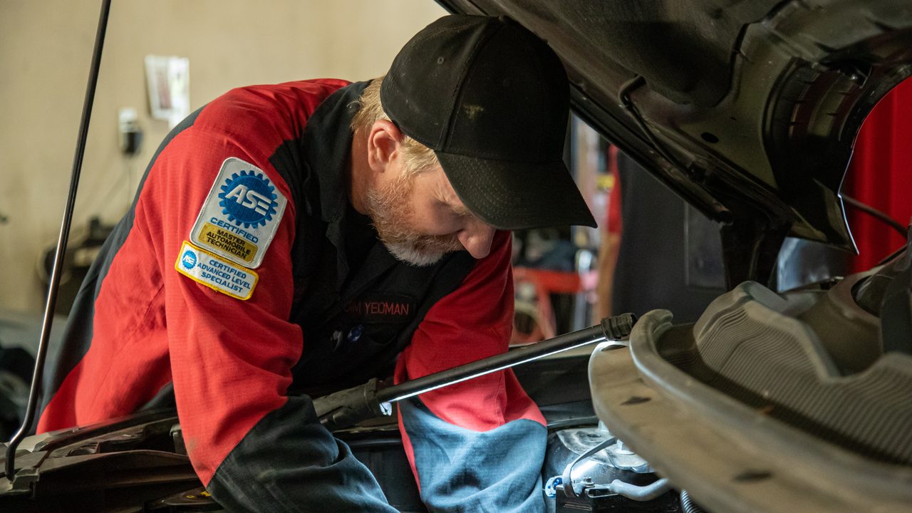 An ASE certified technician inspects and works on vehicle components inside an open engine bay