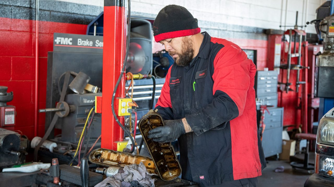 A technician wearing gloves inspects engine valve covers on a work cart inside an automotive repair shop