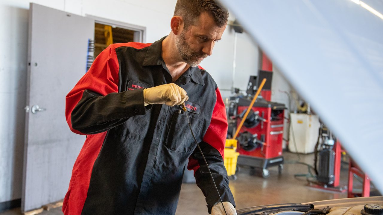 A technician inspects the engine oil dipstick under the hood of a car in a service bay