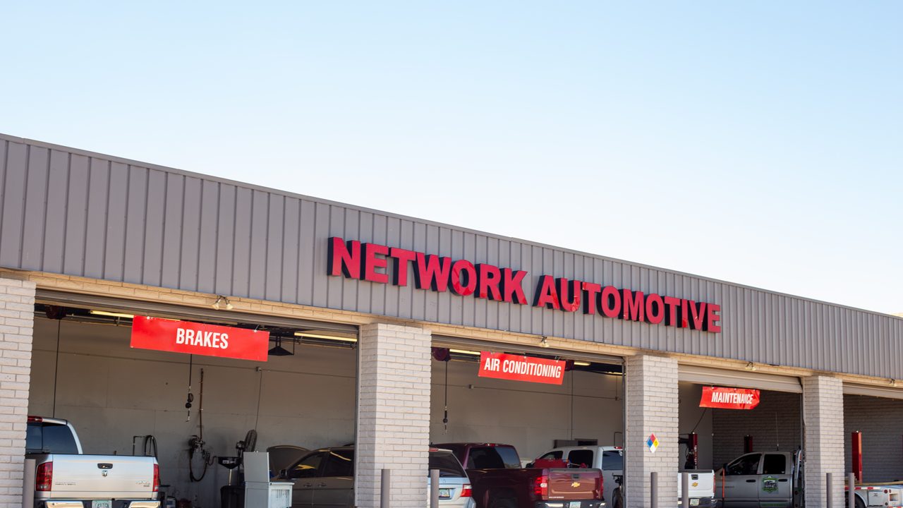 Multiple vehicles are parked inside the open service bays of an automotive repair shop