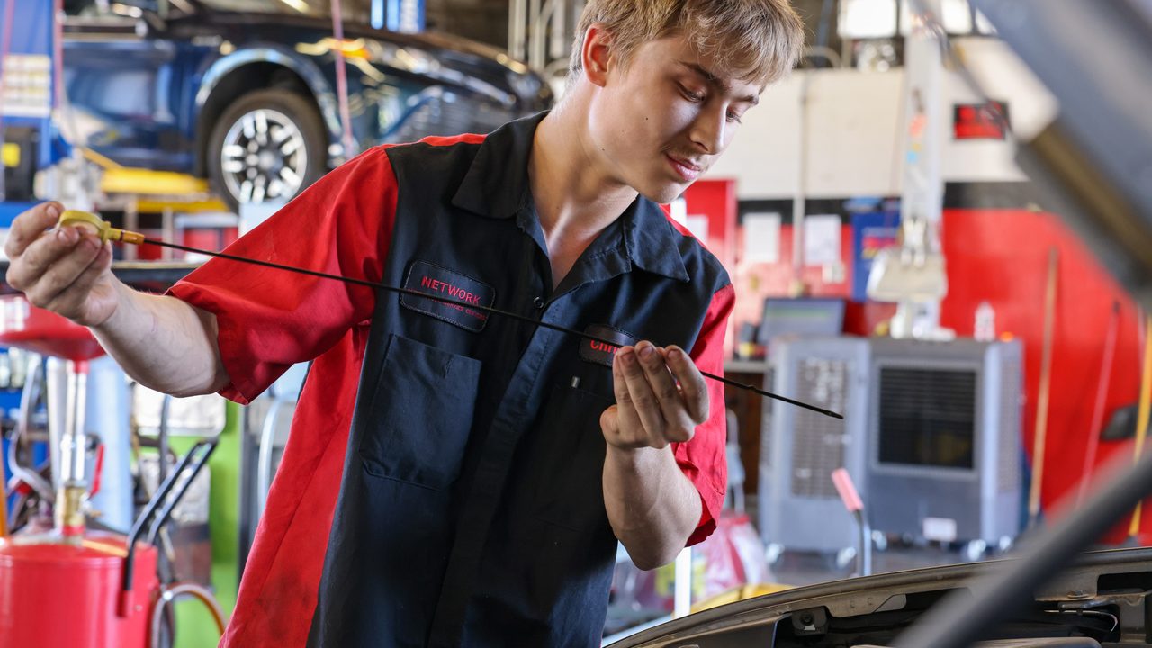 A technician inspects an engine oil dipstick while performing routine maintenance in an auto repair bay