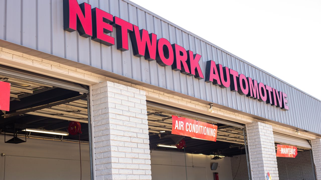 The exterior of an auto repair shop shows branded signage over open service bays with vehicles inside