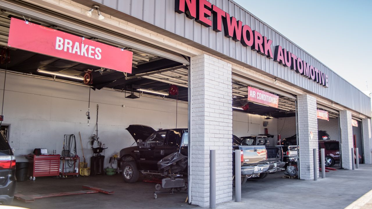 Vehicles sit inside open service bays of an auto repair shop with exterior signage overhead