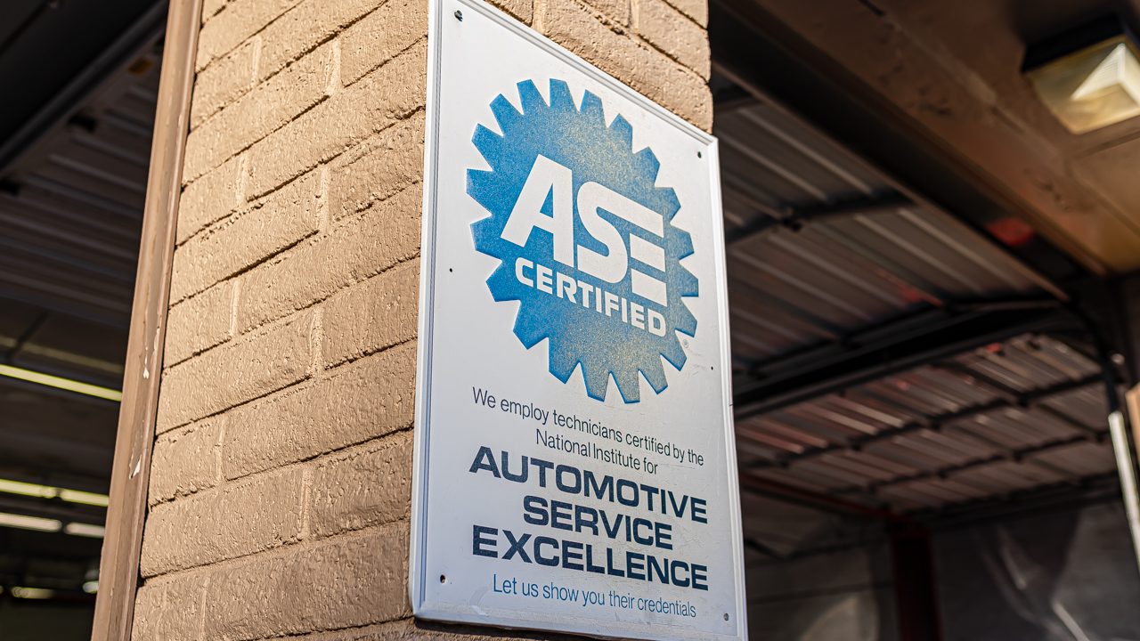 An ASE Certified sign hangs on a brick pillar outside an auto repair shop service bay