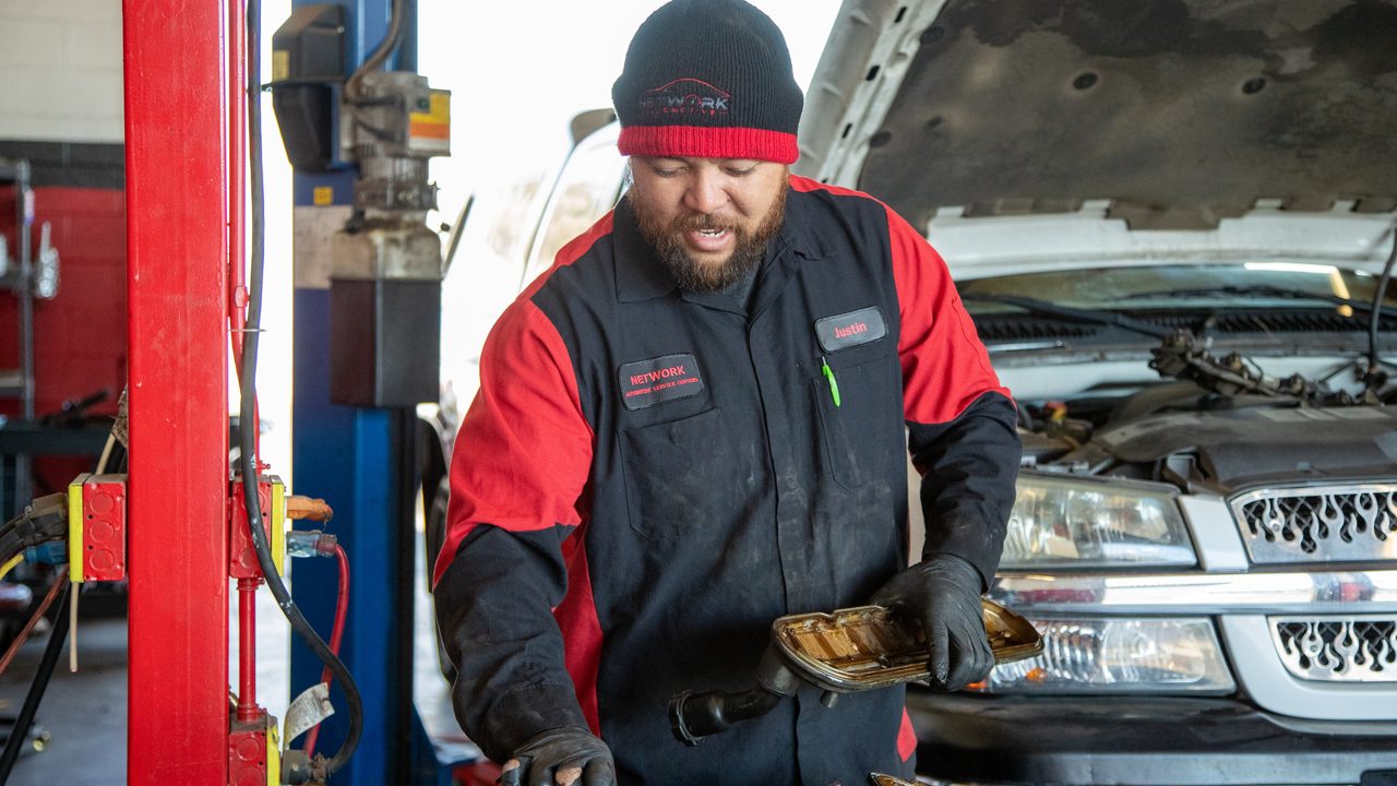 A technician inspects a transmission filter near an open-hood pickup truck on a lift