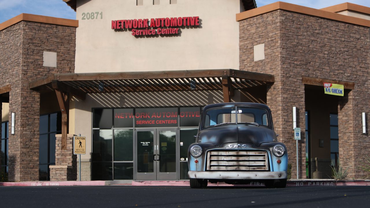 A classic vintage GMC pickup truck is parked in front of an automotive service center storefront