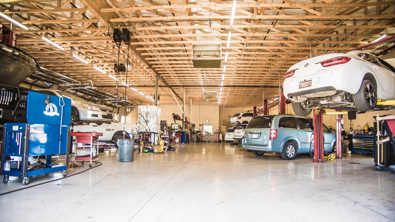 Multiple vehicles sit raised on hydraulic lifts inside a brightly lit, spacious auto repair service bay