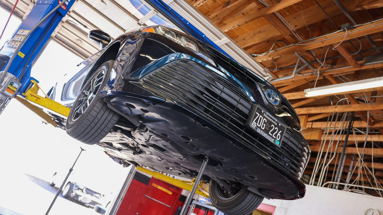 A sedan is elevated on a hydraulic lift inside a service bay for undercarriage inspection