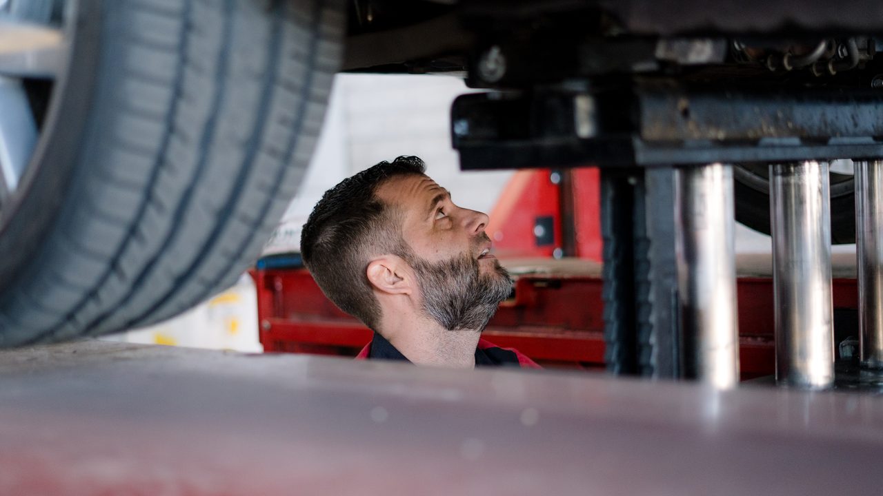 A technician inspects the undercarriage of a car elevated on a lift in a service bay