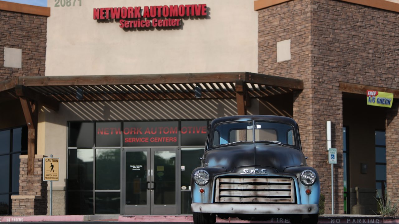 A vintage GMC pickup truck parked outside an automotive service center storefront