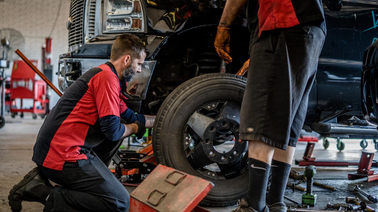 Technicians service the front wheel and suspension on a heavy-duty pickup truck in a repair shop