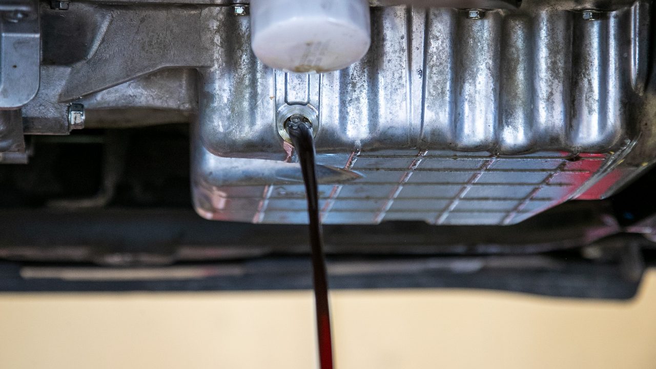 Used motor oil drains from an engine oil pan next to the oil filter during vehicle service