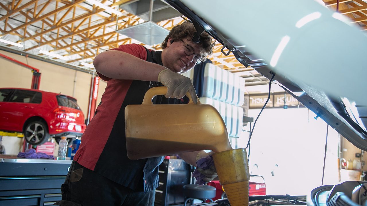 A technician pours fresh motor oil into an engine bay during an oil change in a service bay