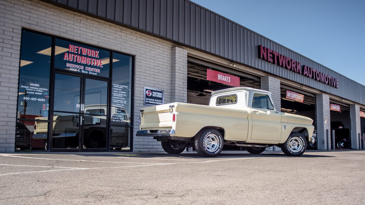A vintage pickup truck is parked outside the service bays of an auto repair shop