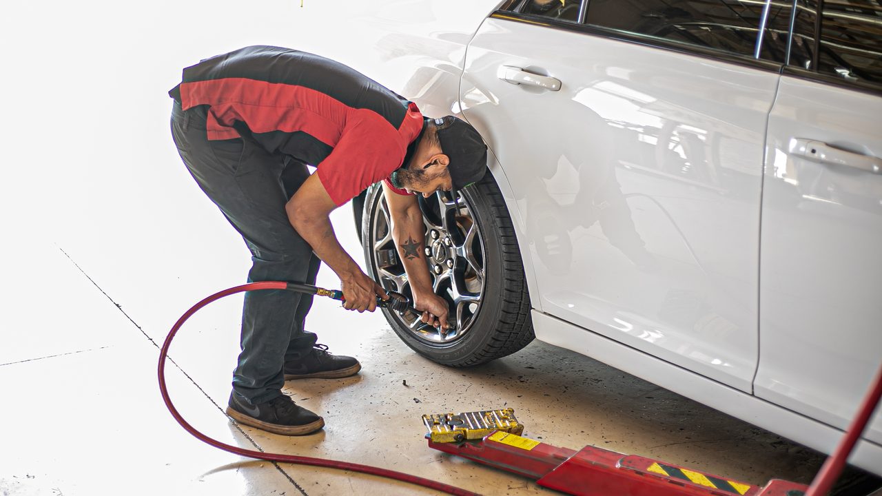 A technician uses an air hose to service a tire on a white sedan in a repair shop