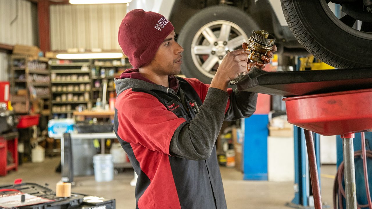 A technician inspects an oil filter while performing an oil change beneath a vehicle on a lift