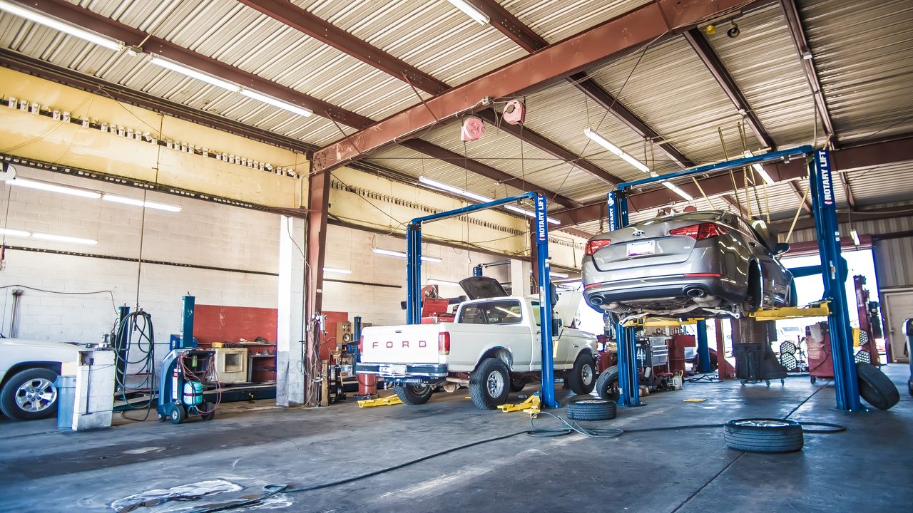 Vehicles are parked and raised on hydraulic lifts inside an auto repair shop service bay