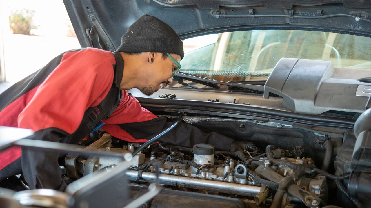 A technician leans into an open engine bay to inspect and service a vehicle engine