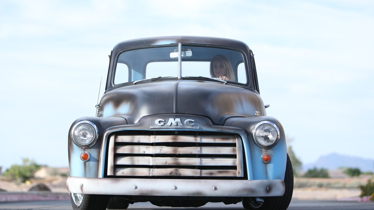 A driver sits behind the steering wheel of a customized classic vintage pickup truck on the road
