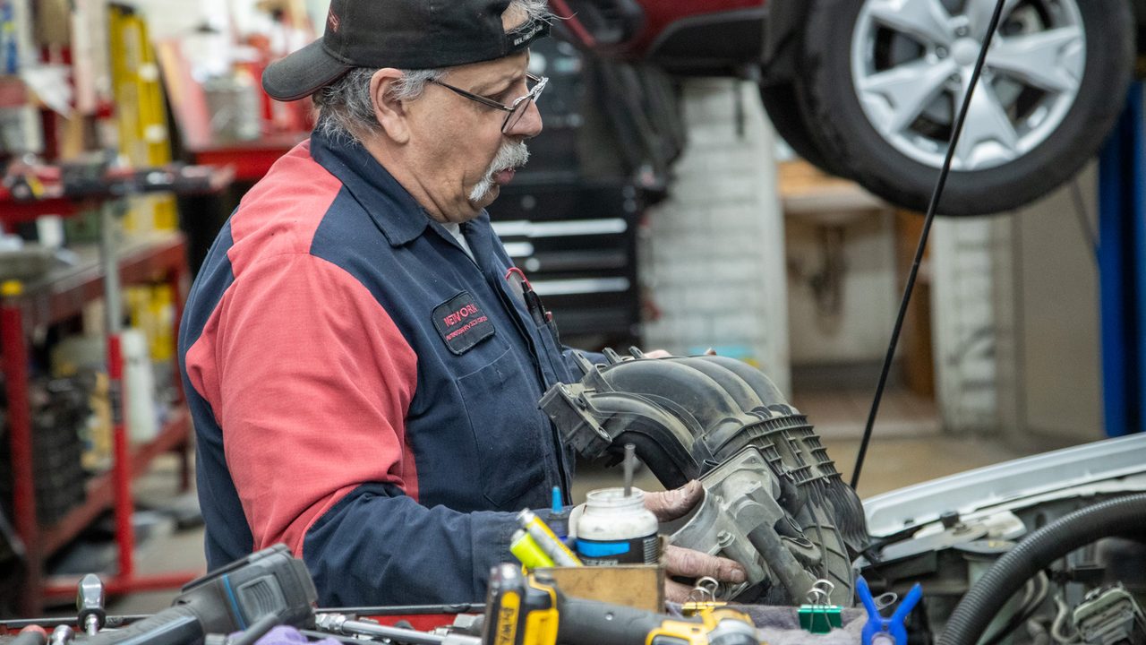 A technician inspects an intake manifold while working on a vehicle in an auto repair shop