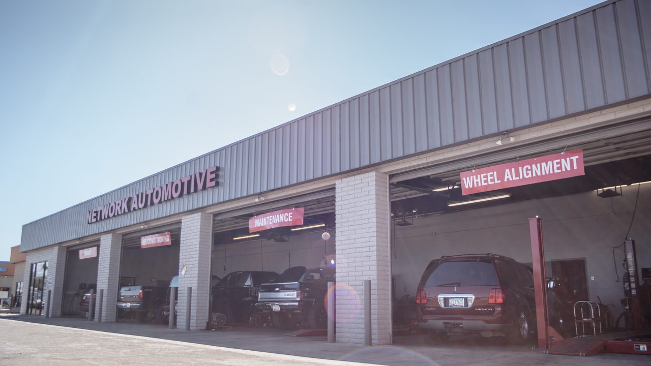 Multiple open service bays at an automotive repair shop house an SUV and trucks undergoing maintenance