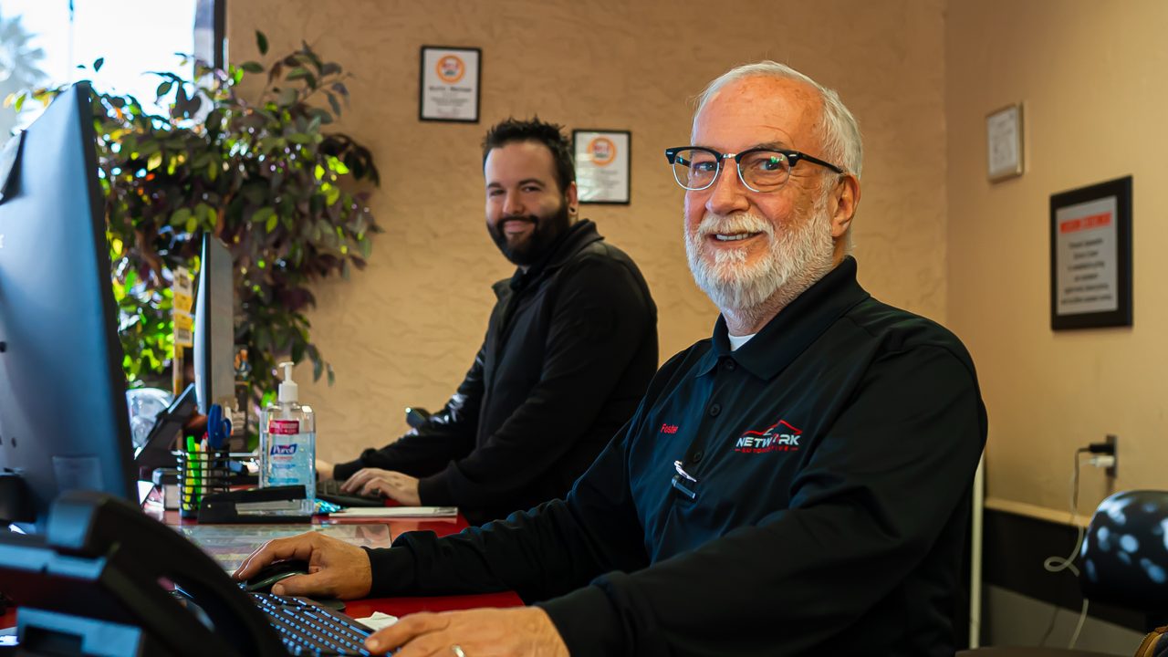 Two service advisors smile while working behind the front counter in an auto repair shop lobby