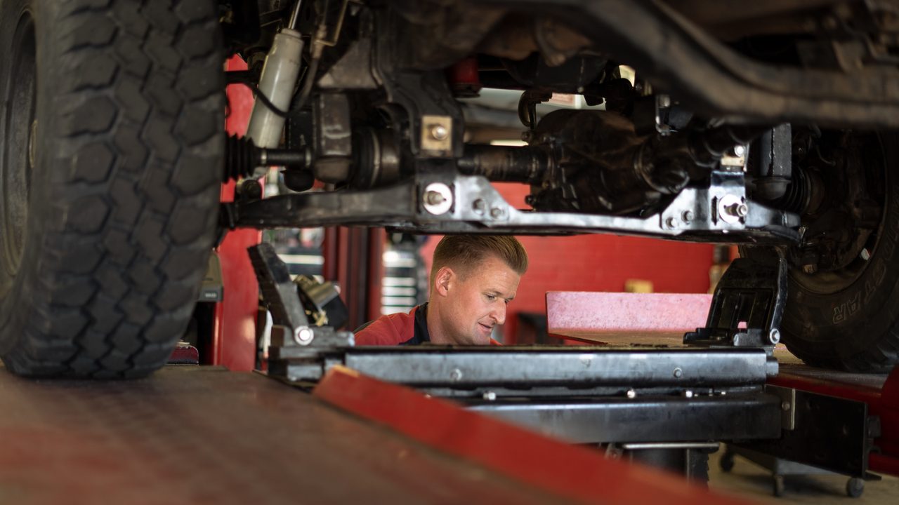 A technician inspects the undercarriage and suspension of a vehicle raised on a lift