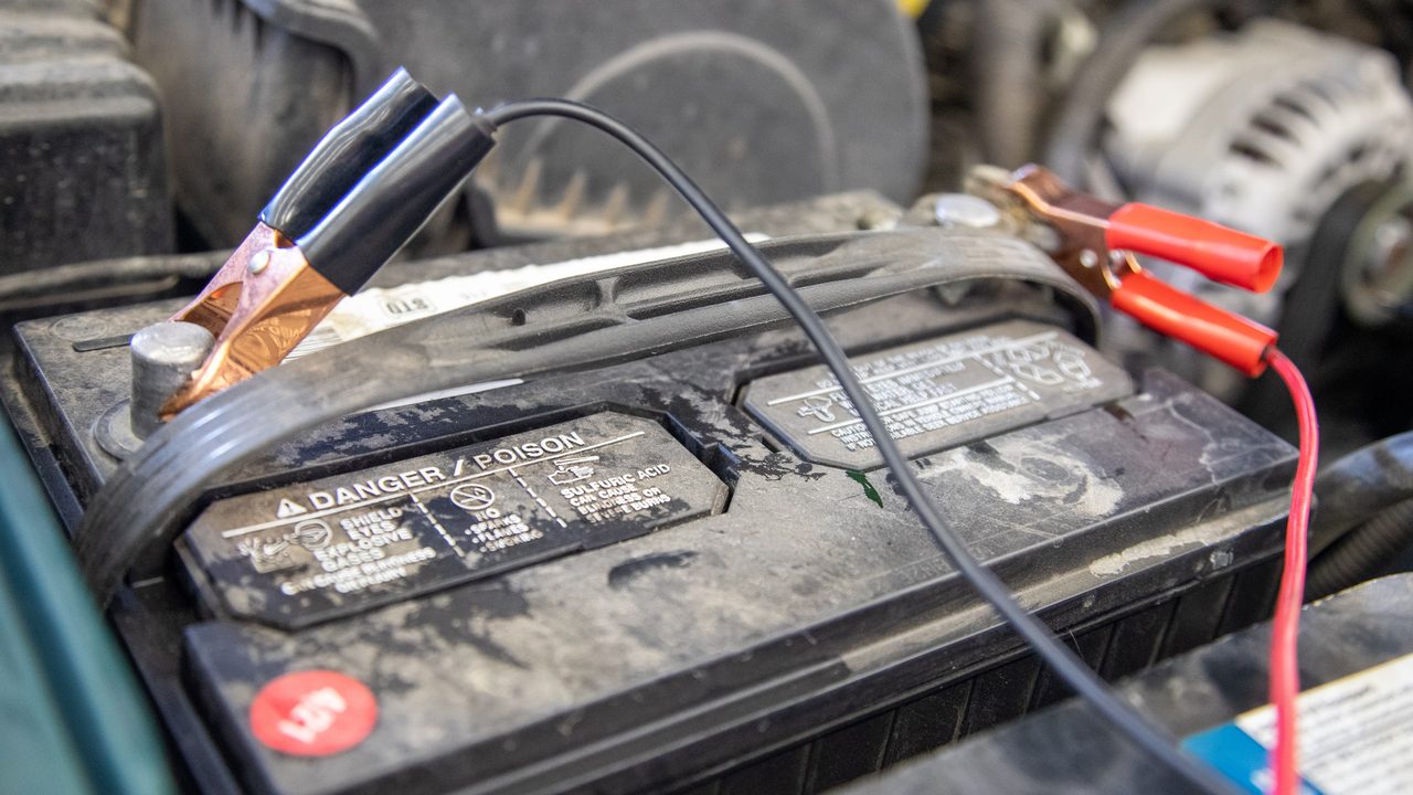 Jumper cable clamps connected to the terminals of a car battery inside an engine bay
