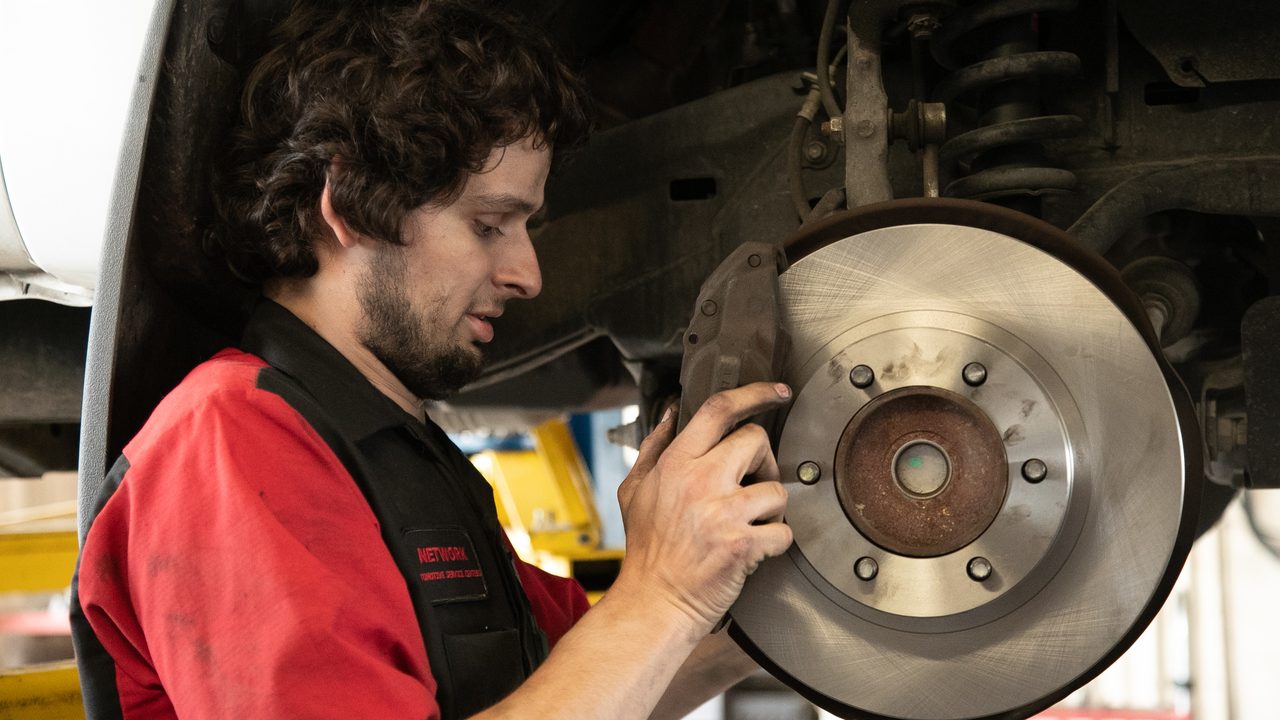 A technician inspects a brake rotor and caliper assembly on a vehicle raised on a lift