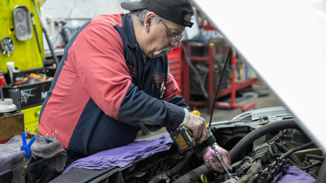 A technician uses a power tool to work on a vehicle engine inside the service bay